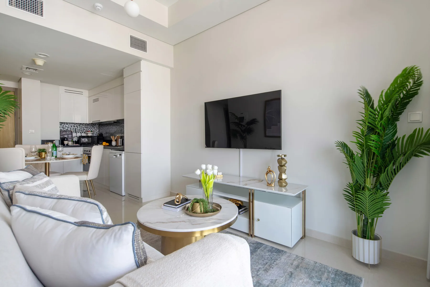 A bright living room with seating, a wall-mounted television, and a dining area.