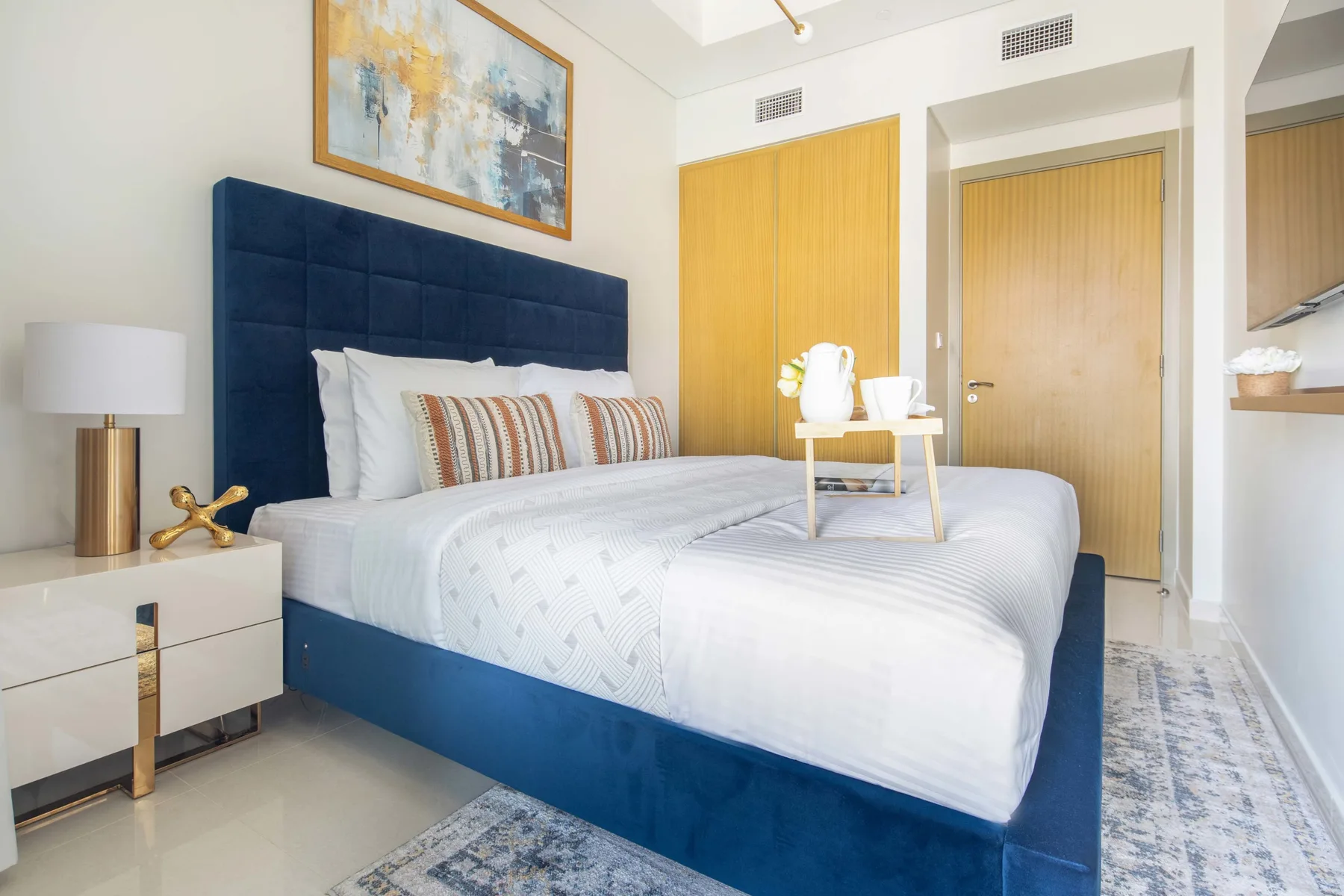 A bedroom with a large bed, navy upholstered headboard, and framed artwork.