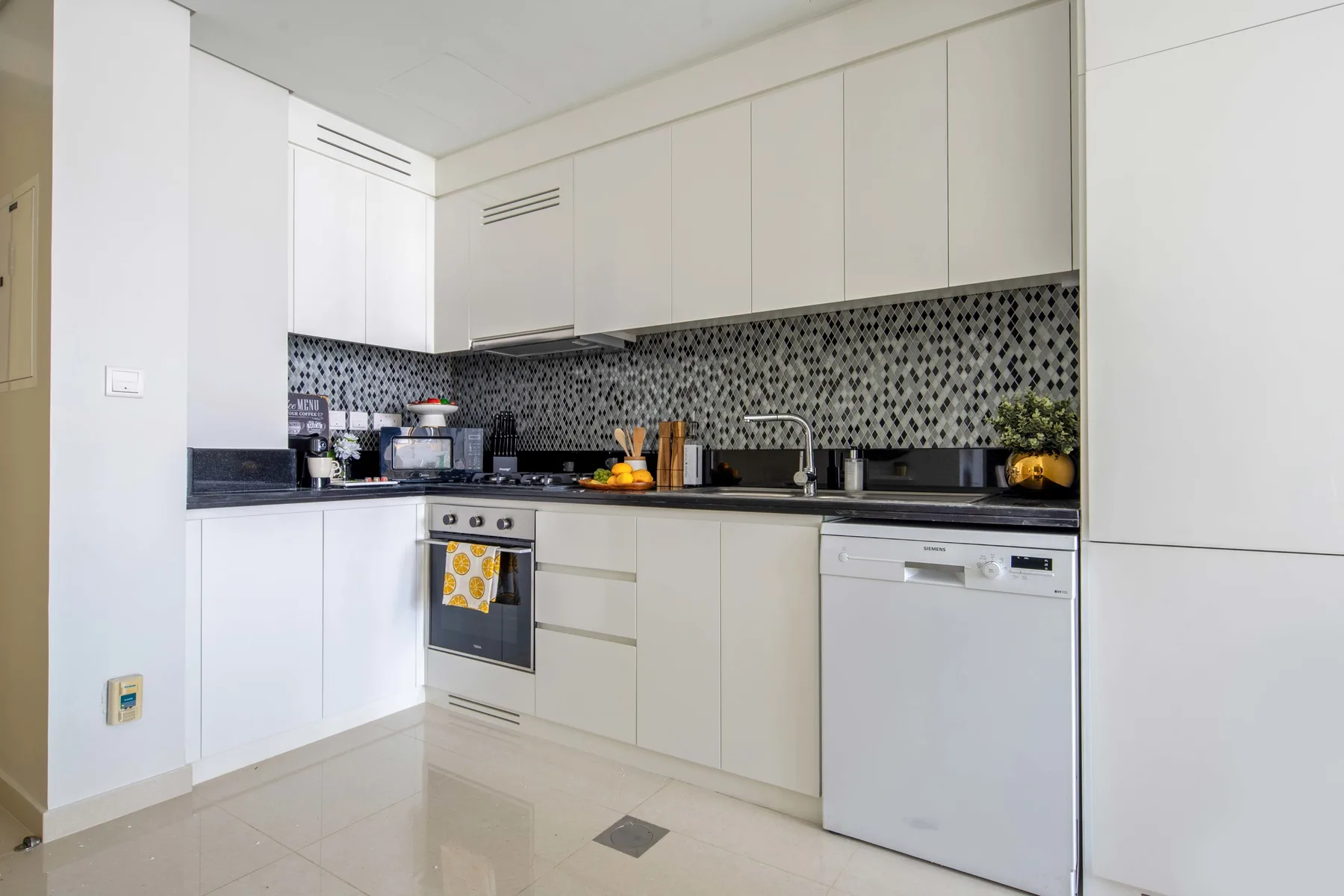A bright kitchen with white cabinets, dark countertops, and a patterned backsplash.