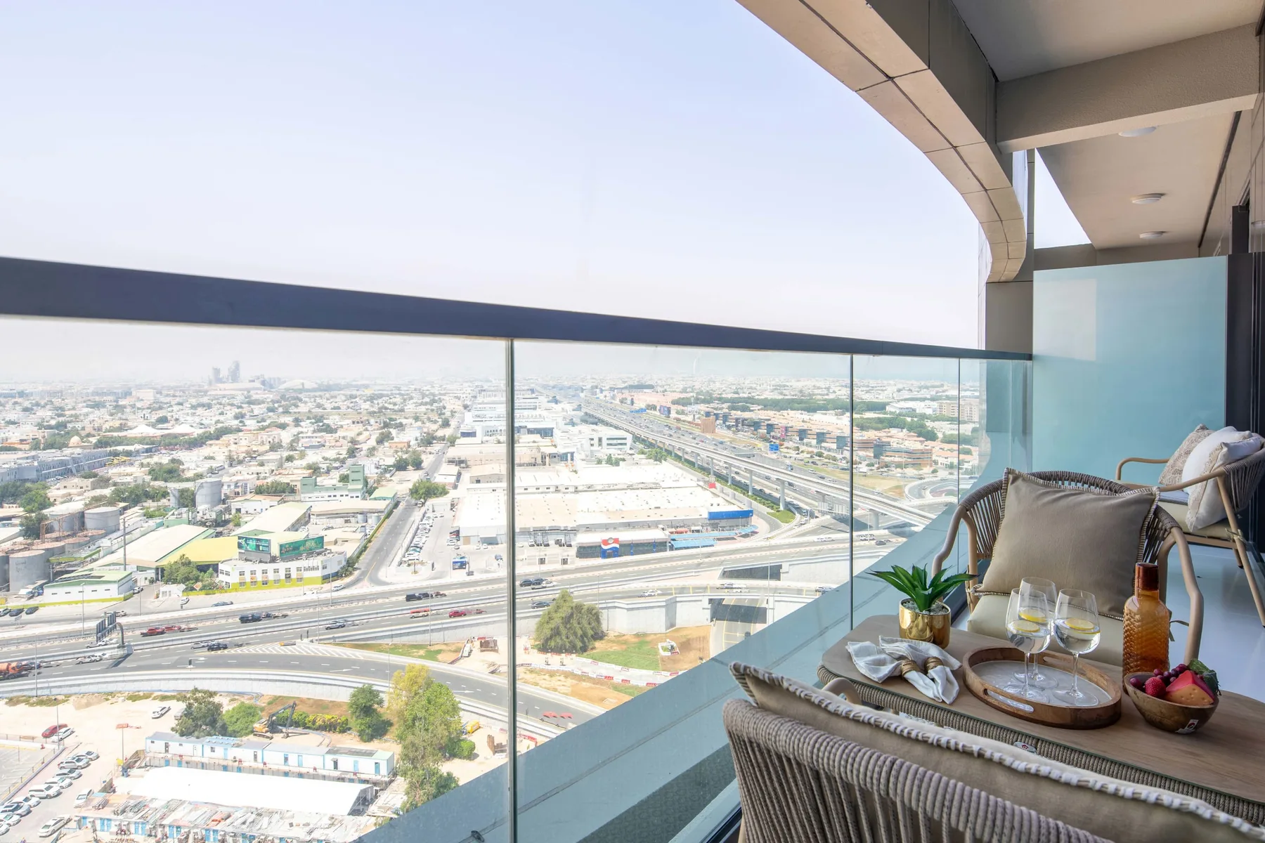 A high-rise balcony seating area overlooks a city and elevated roads.
