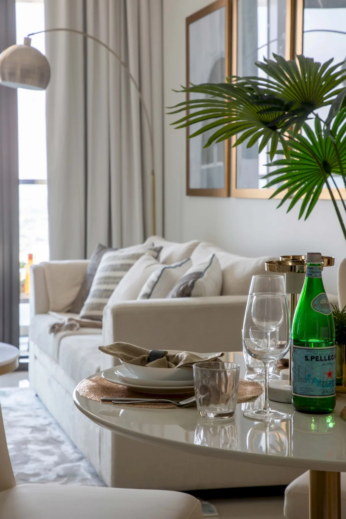 A bright living room with a sofa, a set dining table, and a leafy plant.