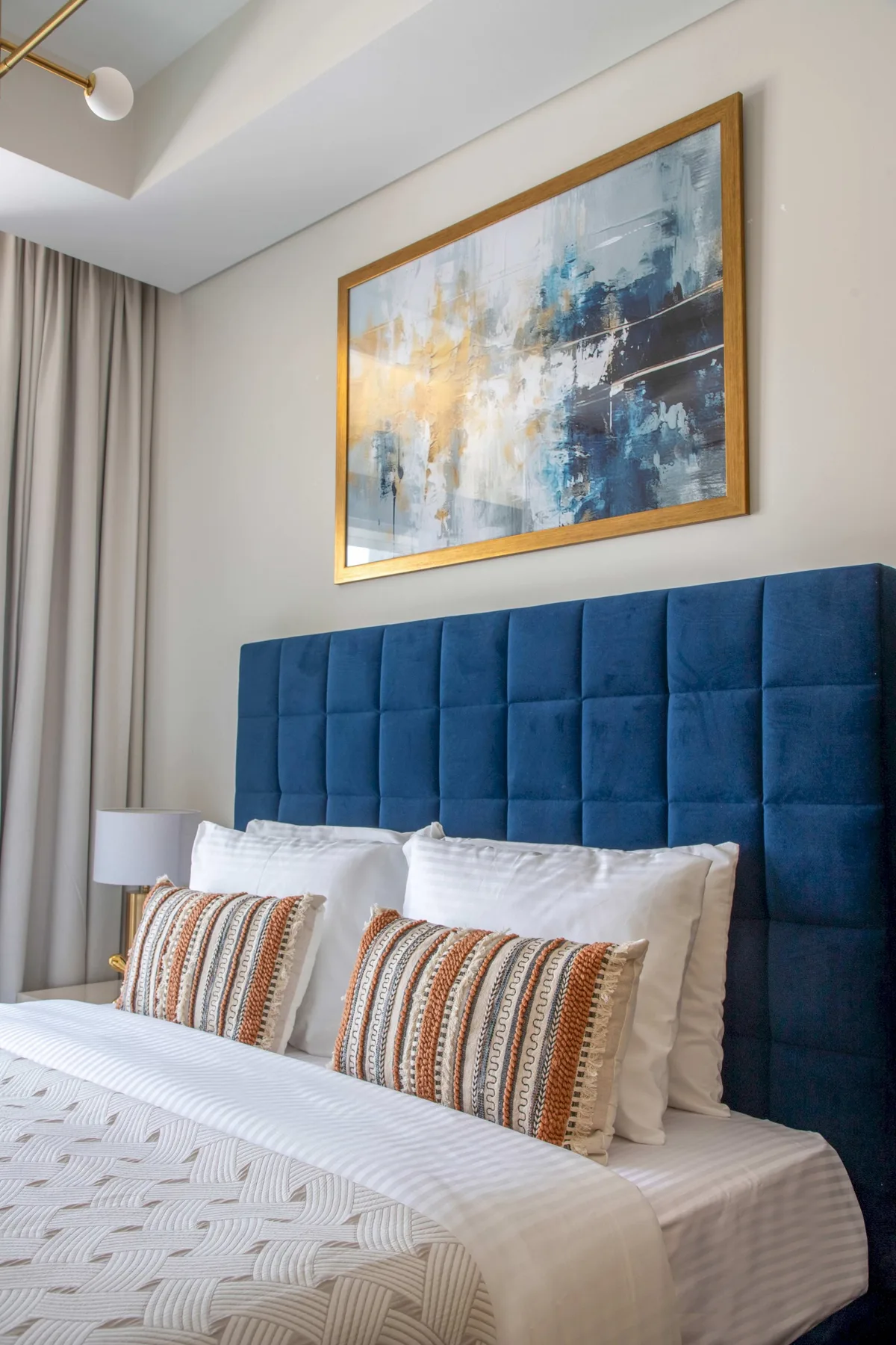 A bedroom with a bed, a blue upholstered headboard, and abstract wall art.