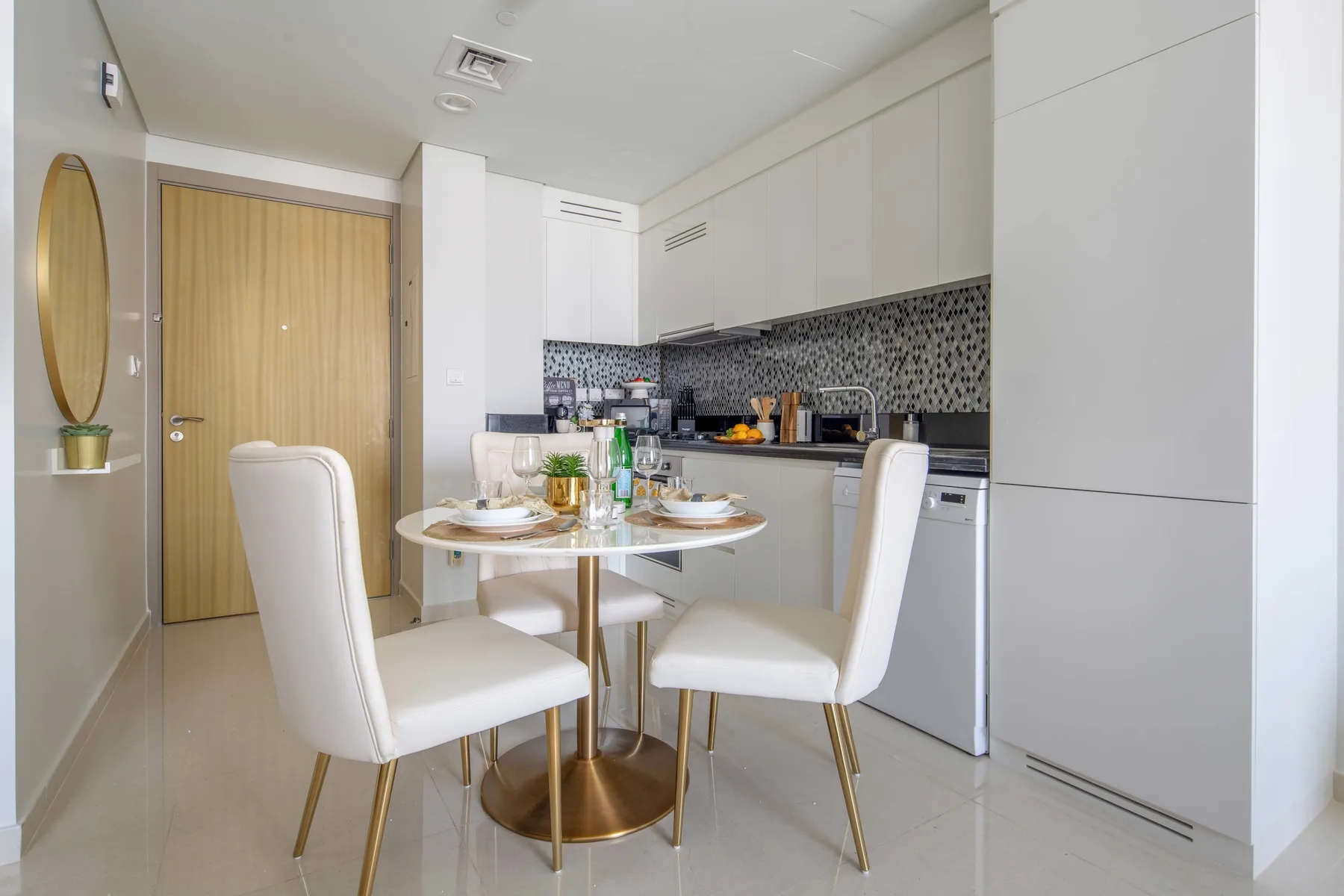 A dining area with a round table and white seating beside a compact kitchen.