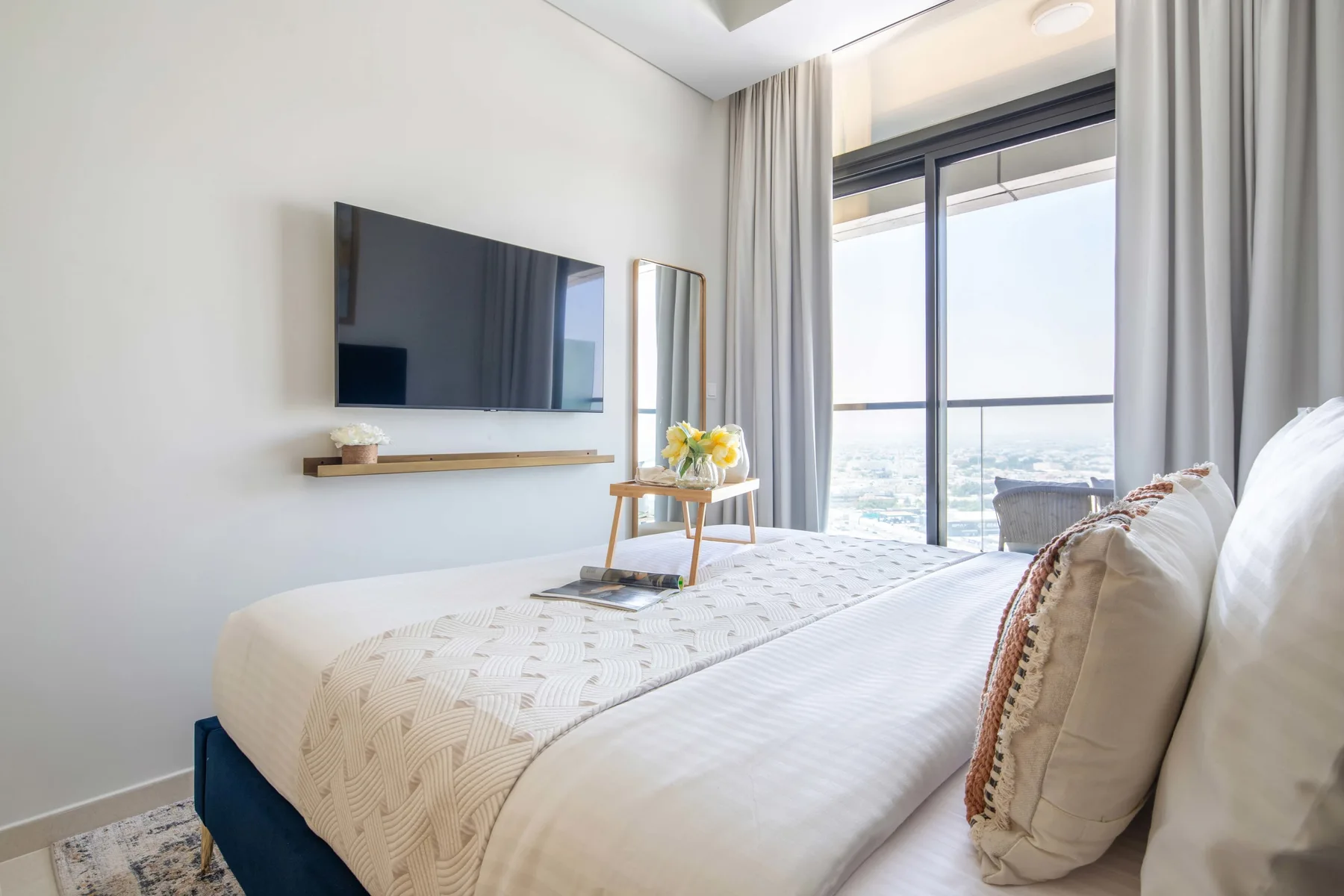A bright bedroom with a neatly made bed beside a large window.