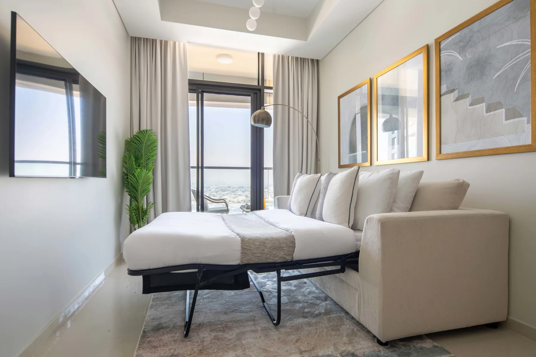 A bright bedroom with a bed, large windows, and framed artwork.