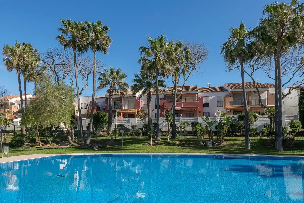 Una piscina con palmeras y edificios residenciales al fondo.