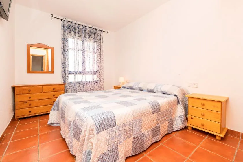 Un dormitorio con una cama, mesitas a juego y una ventana con cortinas estampadas.