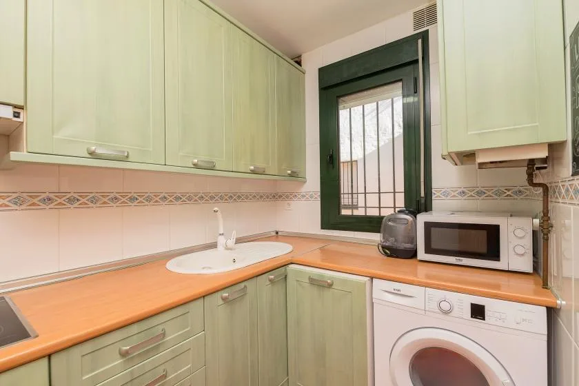 Una cocina compacta con gabinetes verdes, encimeras naranjas y una ventana sobre el fregadero.