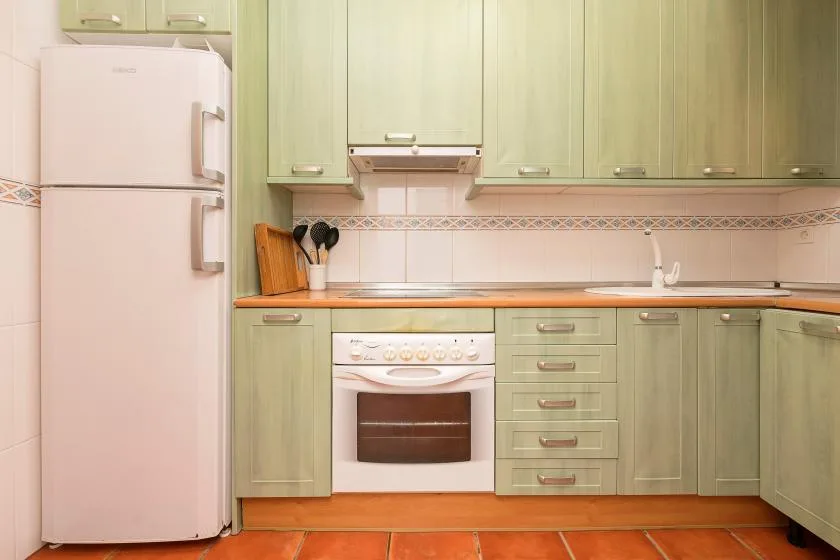 Una cocina con gabinetes verdes, un refrigerador y un horno integrado.