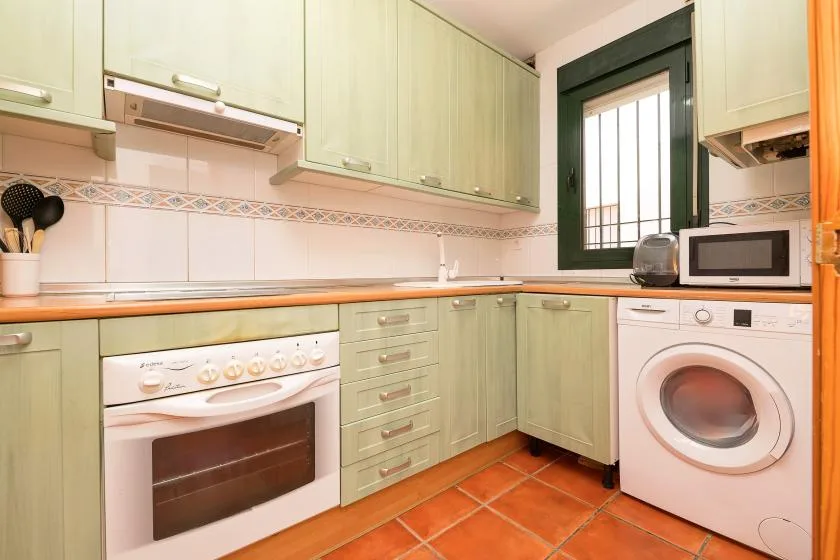 Una cocina con gabinetes verde claro, una estufa y una lavadora.