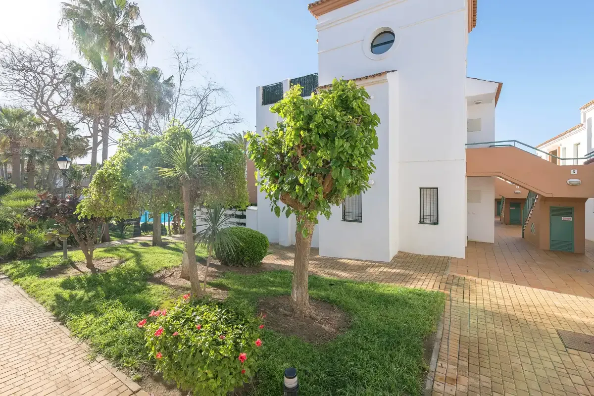 Un edificio blanco junto a un jardín ajardinado y un camino pavimentado.