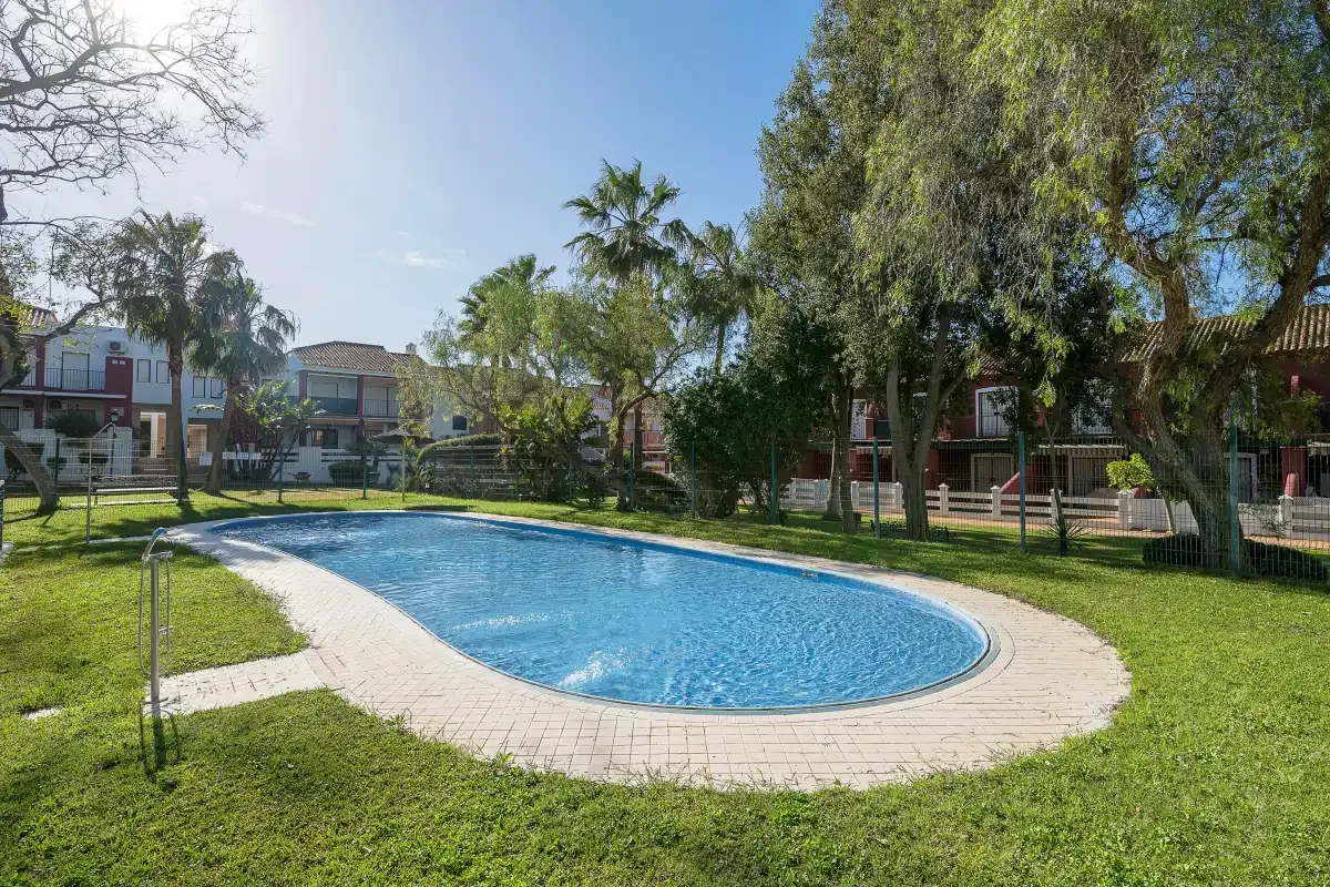 Una piscina exterior curva está rodeada de césped y árboles.