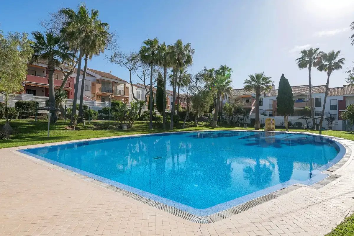 Una piscina exterior luminosa está rodeada de palmeras y edificios residenciales.