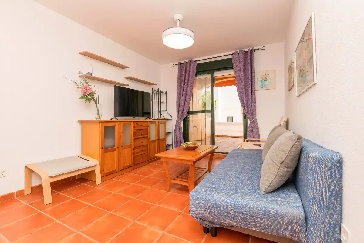 Una sala de estar con asientos azules, una mesa de centro de madera y cortinas moradas.