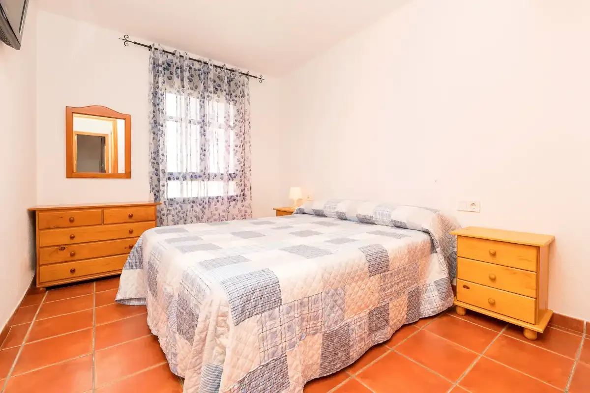 Un dormitorio con una cama, cómodas de madera y una ventana con cortinas.