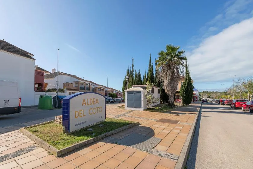 Una calle residencial soleada con un letrero del vecindario junto a la acera.