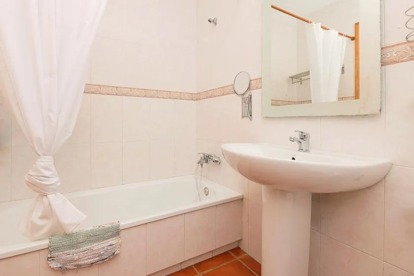 Un baño alicatado con bañera, cortina de ducha y lavabo de pared.