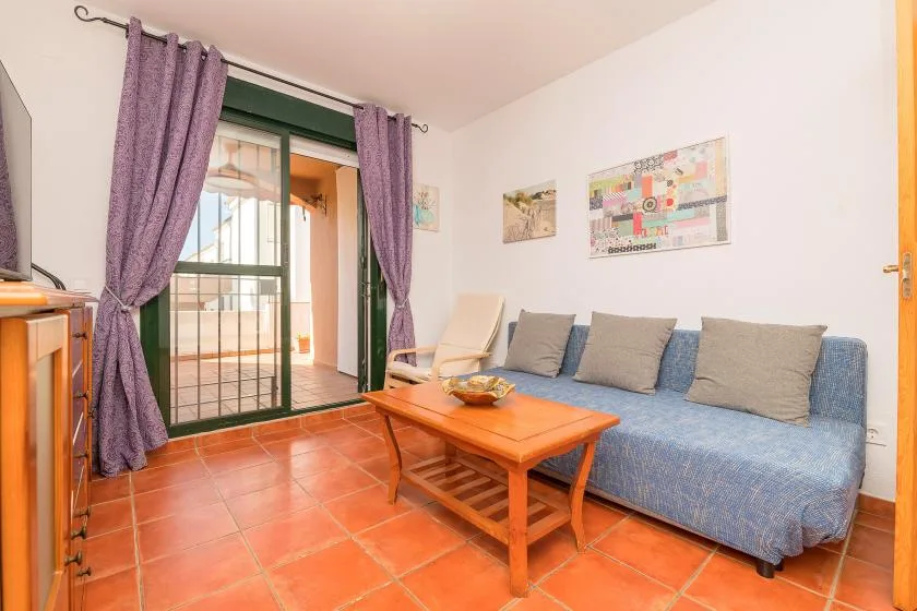 Una sala de estar con asientos azules, una mesa de centro de madera y puertas de vidrio.