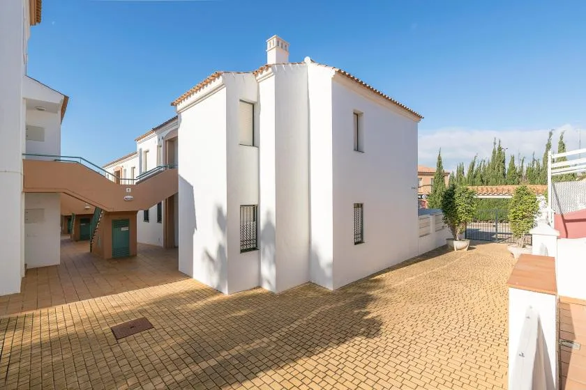 Un edificio blanco da a un patio pavimentado y soleado.