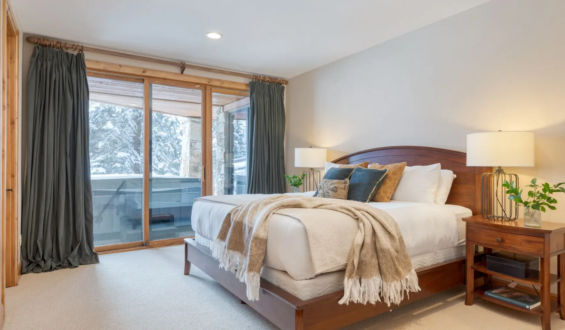 Un dormitorio con una cama bien tendida junto a puertas de cristal y cortinas oscuras.