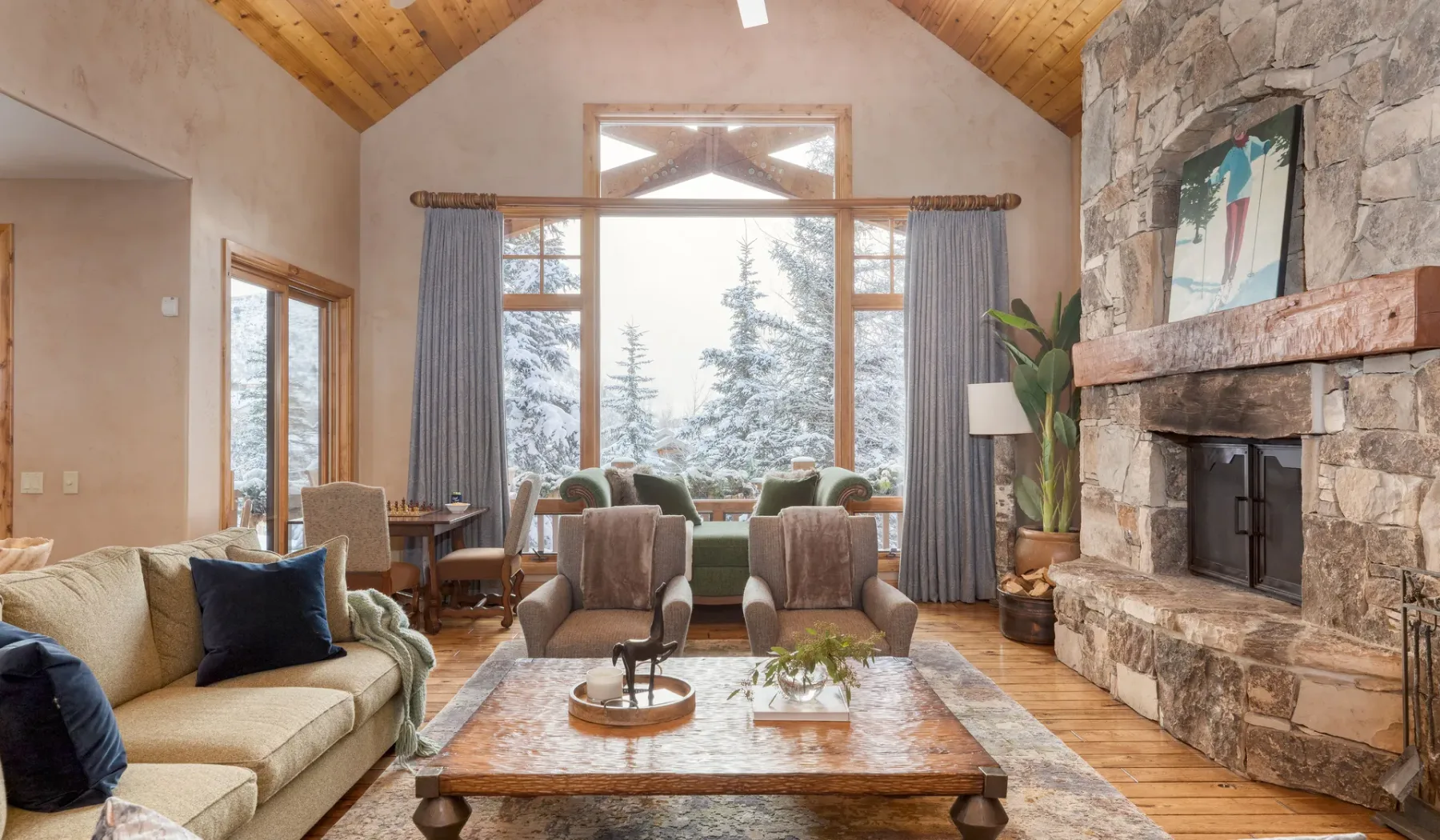 Una sala de estar con asientos, una chimenea de piedra y grandes ventanales con vista a los árboles.