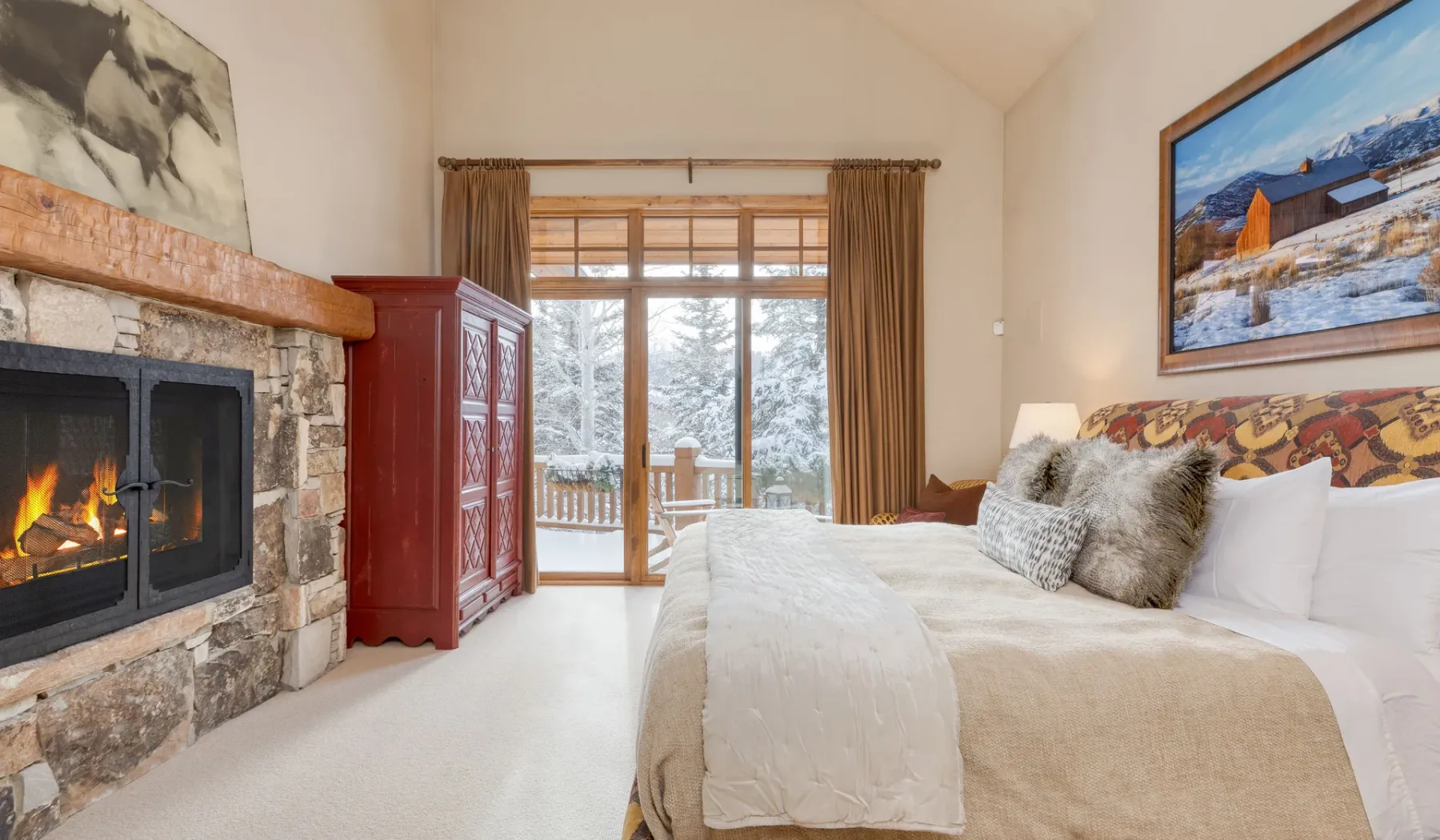 Un dormitorio con una cama grande junto a una chimenea de piedra y puertas de vidrio.