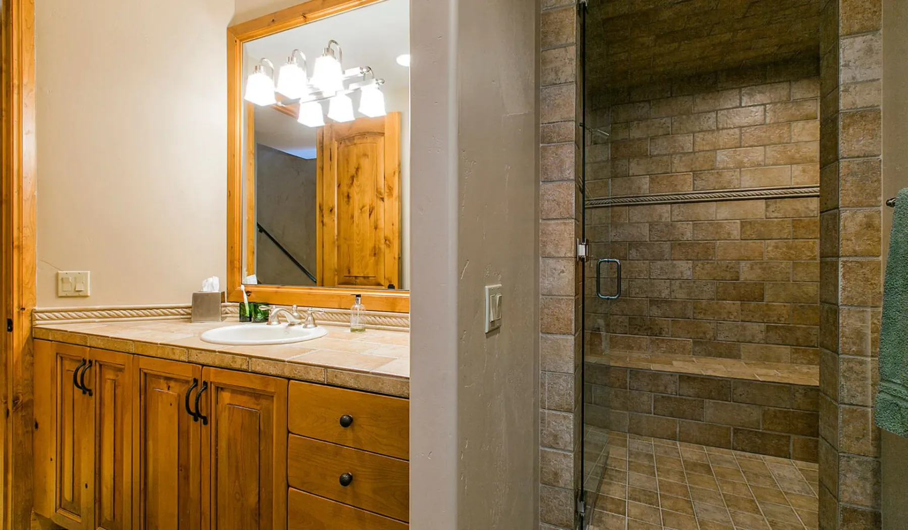 Un tocador de baño con espejo está junto a una ducha revestida de azulejos.