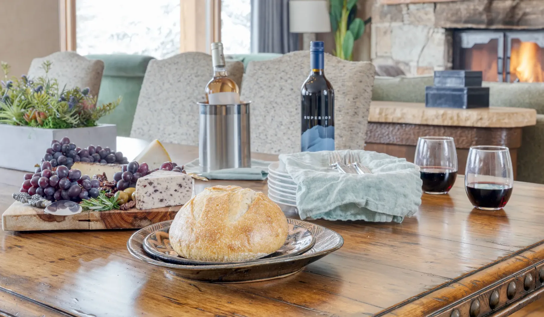 Una mesa de comedor está puesta con pan, fruta, vino y servilletas dobladas.