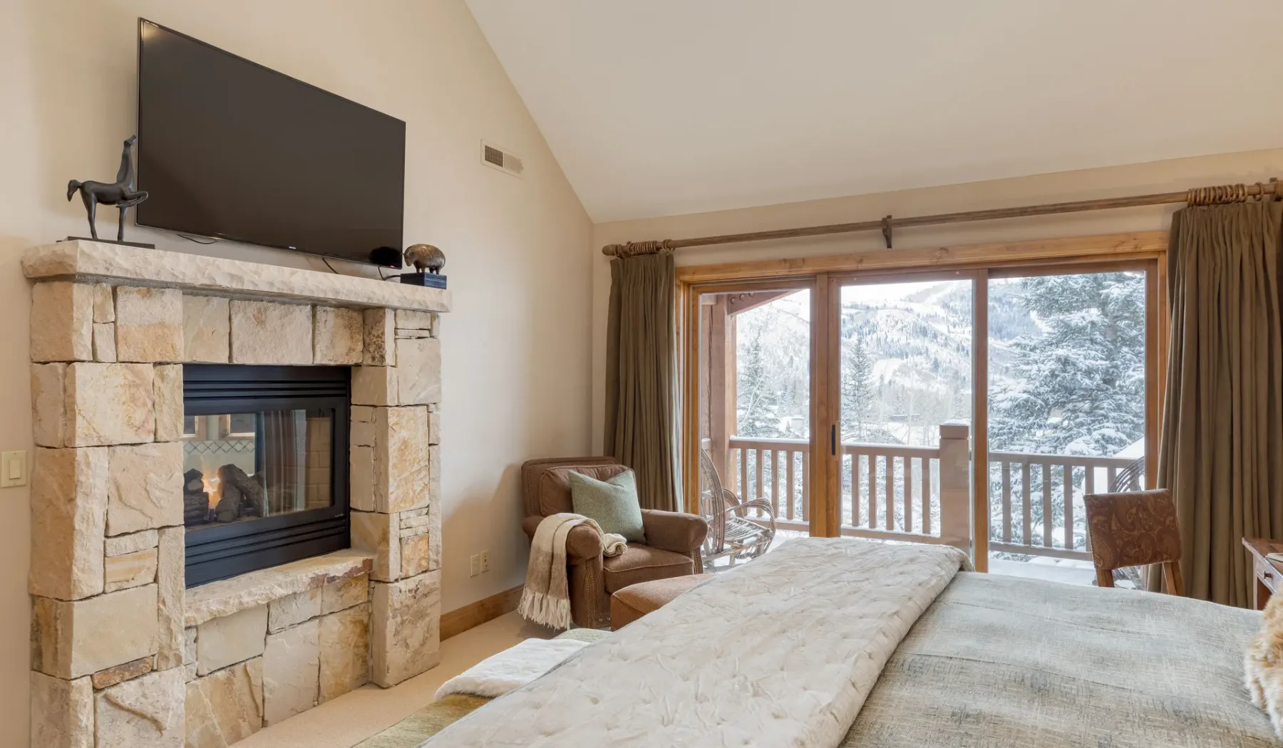 Un dormitorio con chimenea de piedra, cama y grandes ventanas con vistas a un paisaje nevado.