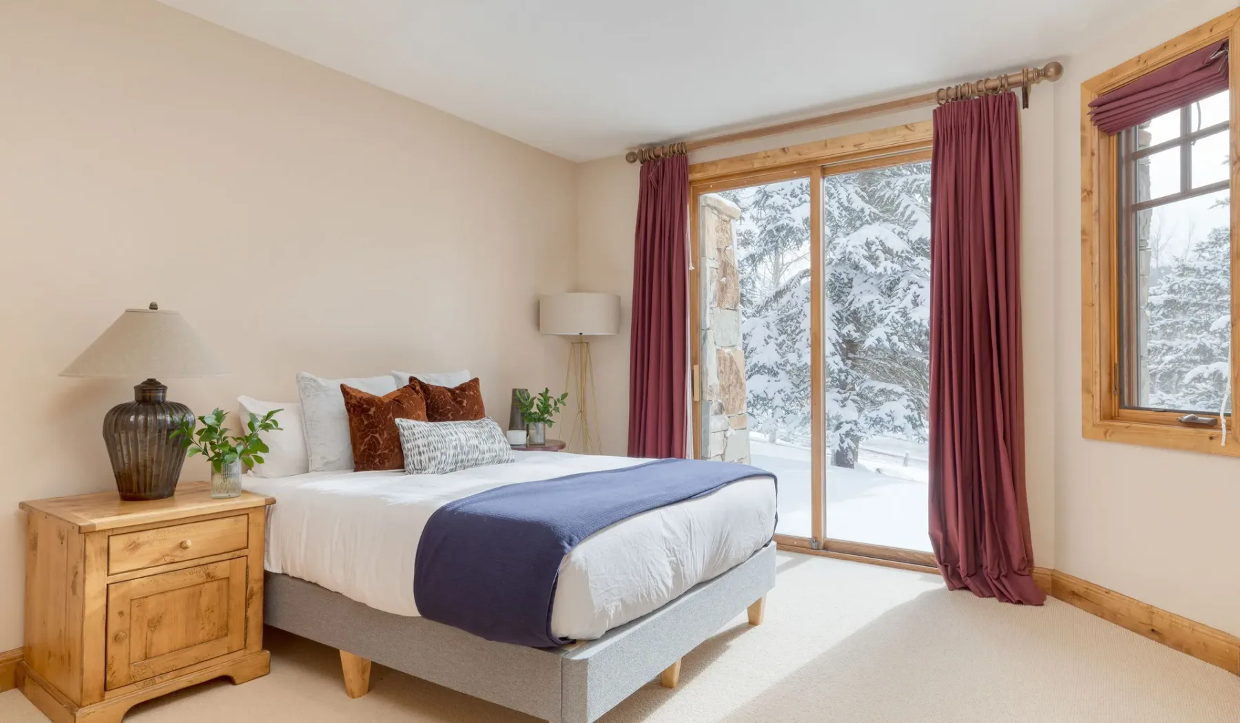 Dormitorio con una cama bien tendida y grandes ventanas con vistas a un paisaje nevado.