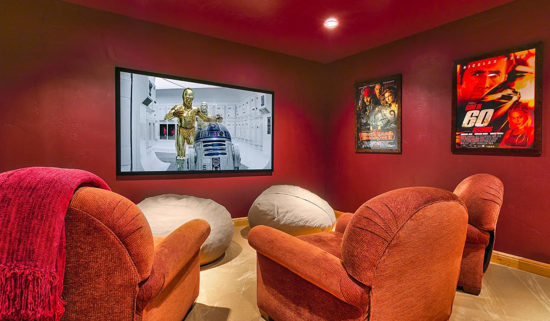 Una sala de cine en casa con paredes rojas, asientos mullidos y una película en pantalla.