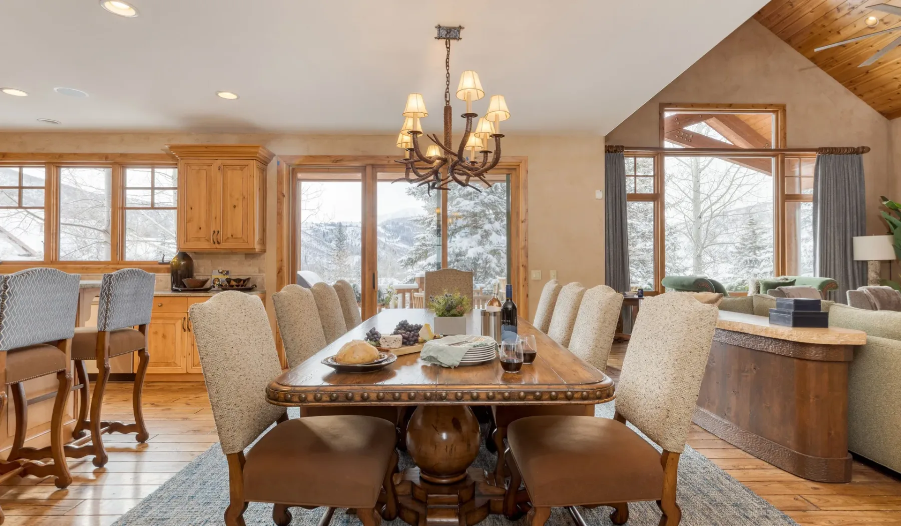 Comedor con una mesa de madera junto a una cocina y grandes ventanas.