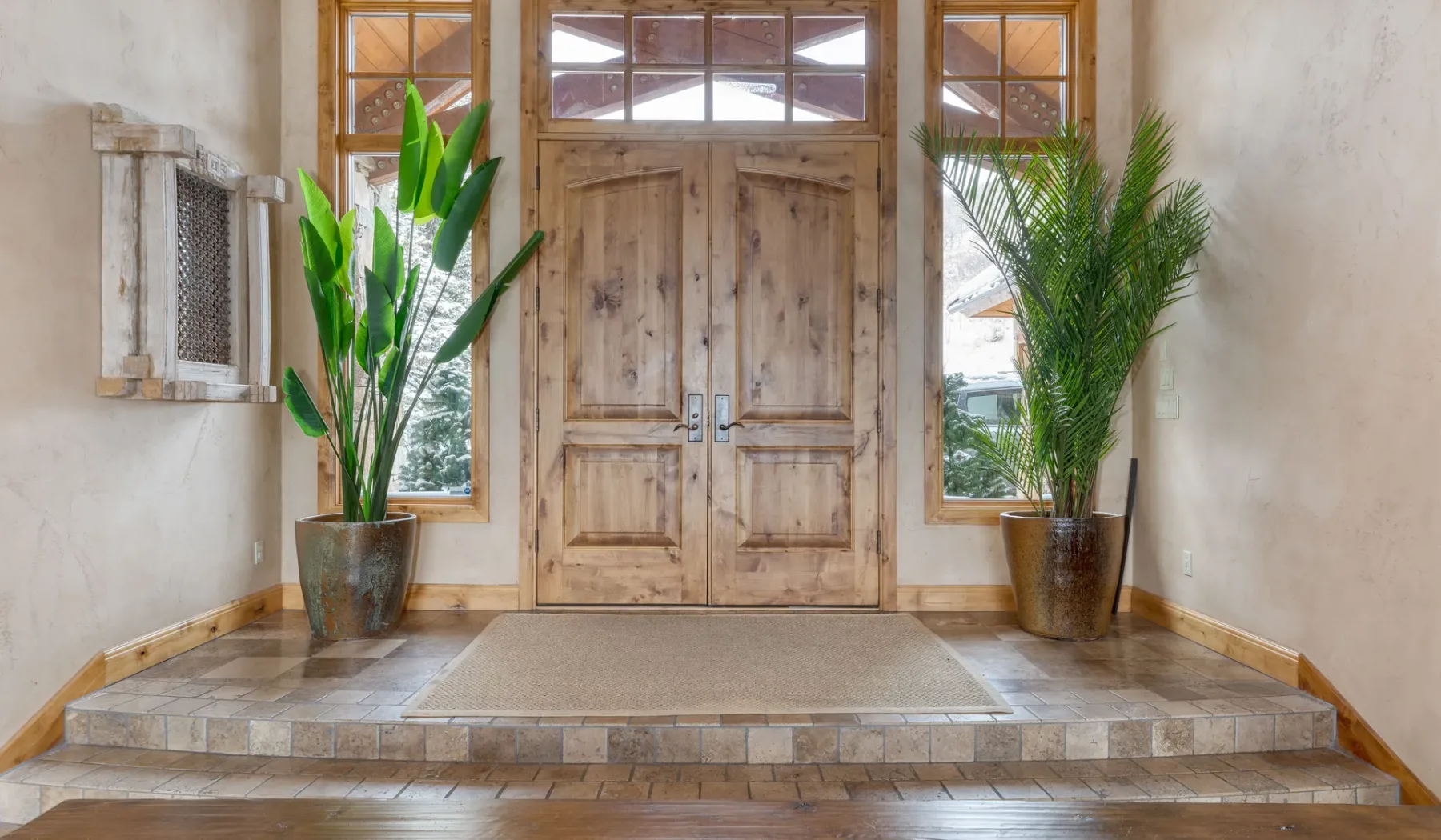Una entrada luminosa presenta puertas dobles de madera y plantas en macetas.