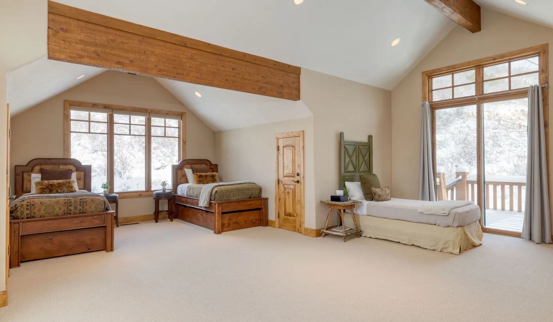 Un dormitorio luminoso con dos camas de madera y una cama individual junto a una ventana grande.