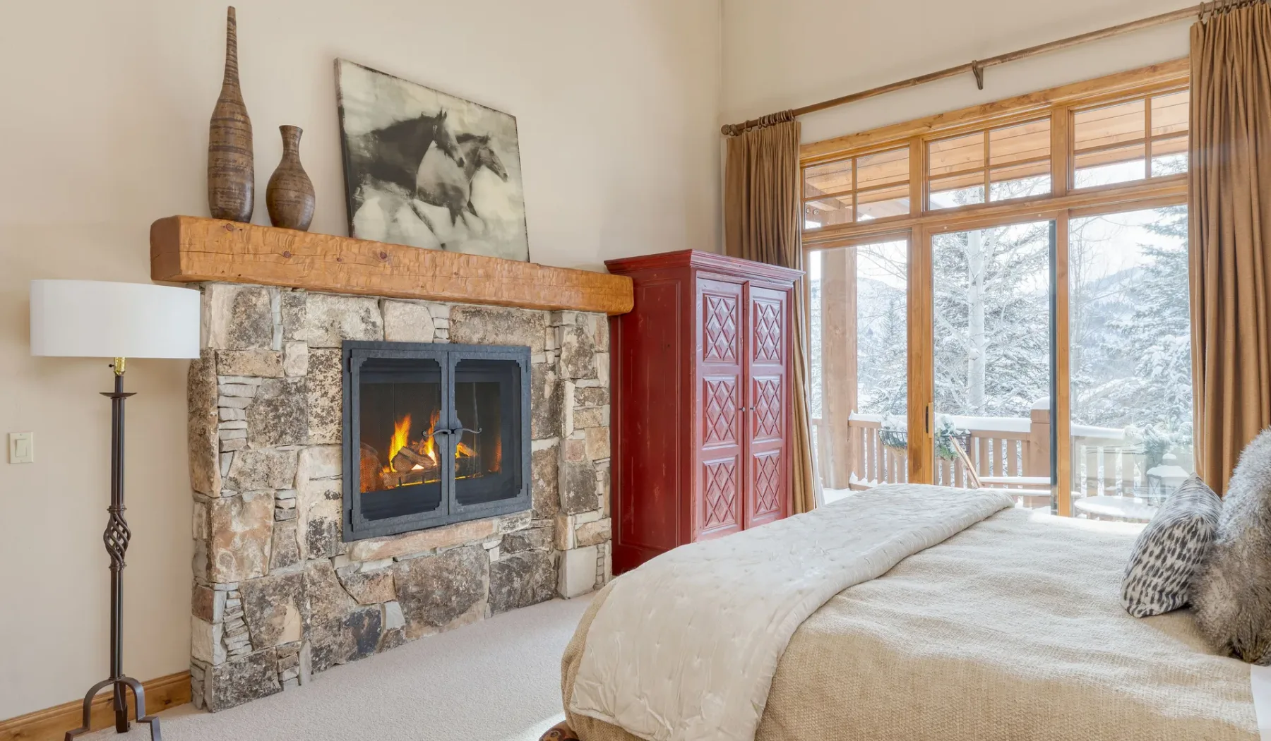 Un dormitorio con chimenea de piedra, una cama y grandes ventanas que dan a un balcón.