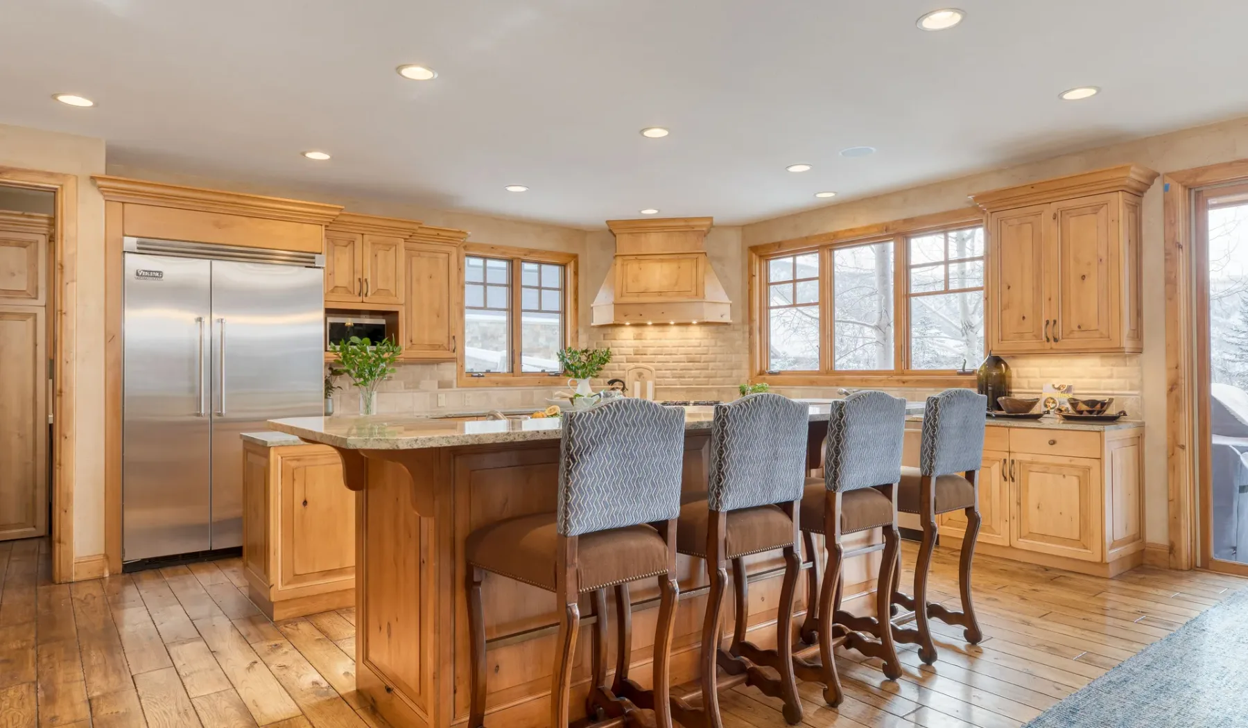 Una cocina luminosa con una isla central, asientos de barra y ventanas grandes.