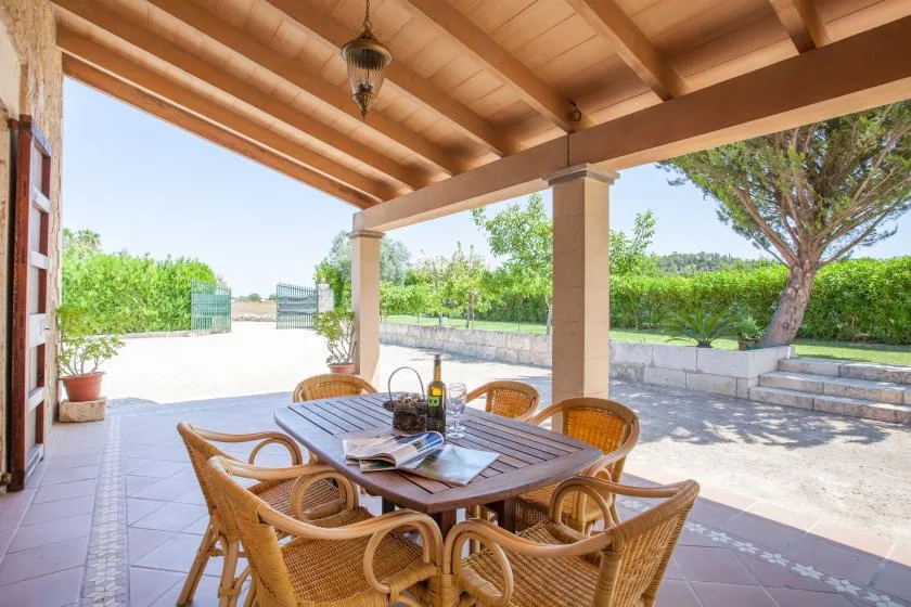 A covered outdoor dining area with a wooden table and woven seating.