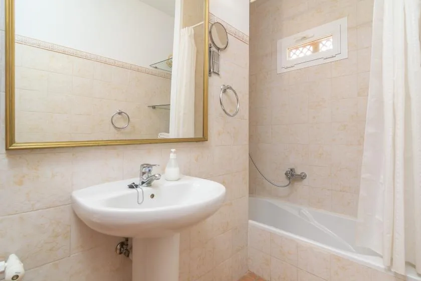 A tiled bathroom with a sink, large mirror, and bathtub behind a shower curtain.