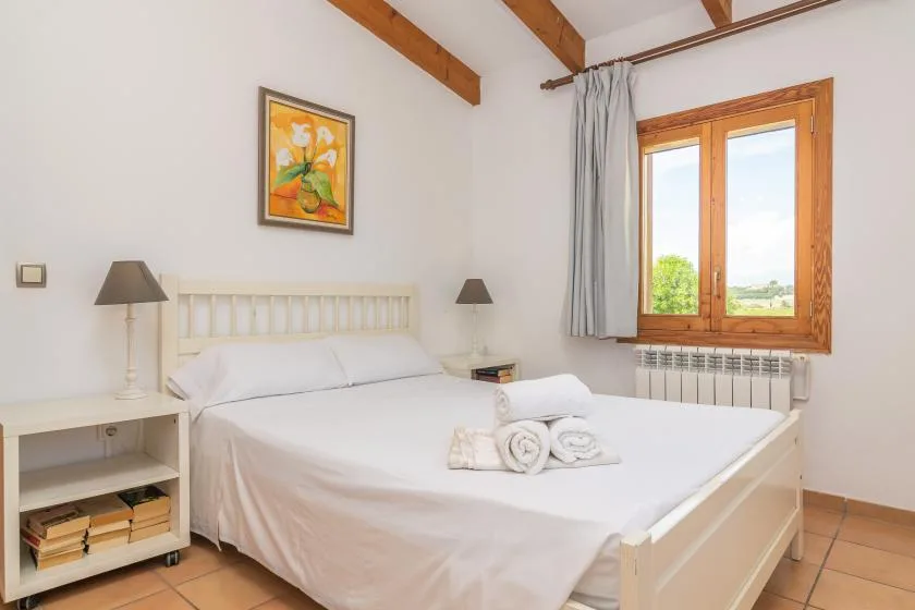 A bedroom with a neatly made bed, bedside tables, and a wooden-framed window.