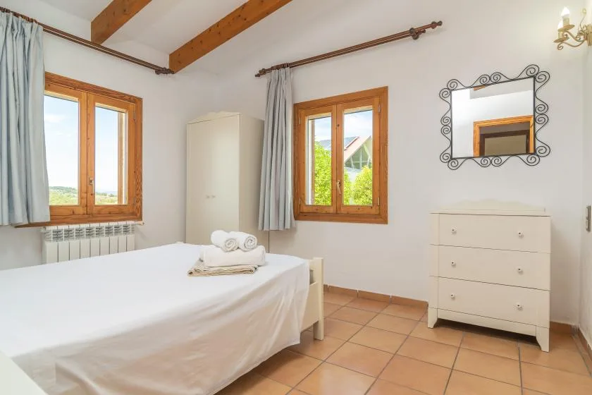 A bedroom with a bed, two windows, and a chest of drawers.