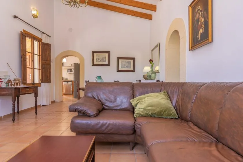 A living room with brown seating, a wooden window, and exposed ceiling beams.