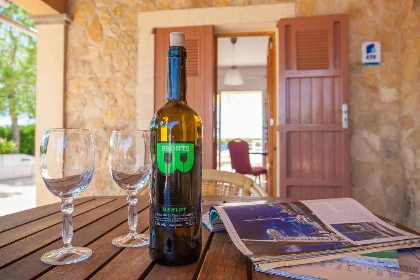 A bottle, wine glasses, and brochures sit on a wooden table outside an open doorway.