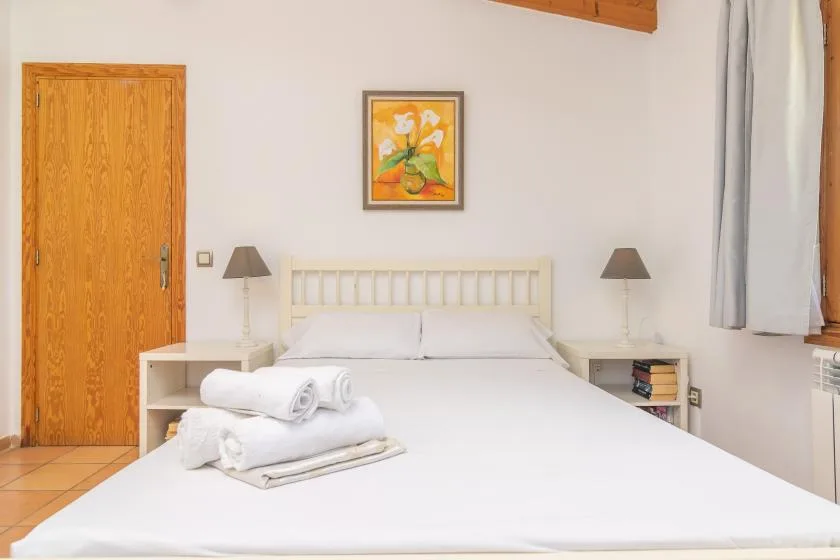 A bedroom with a white bed, bedside tables, and a framed floral picture.