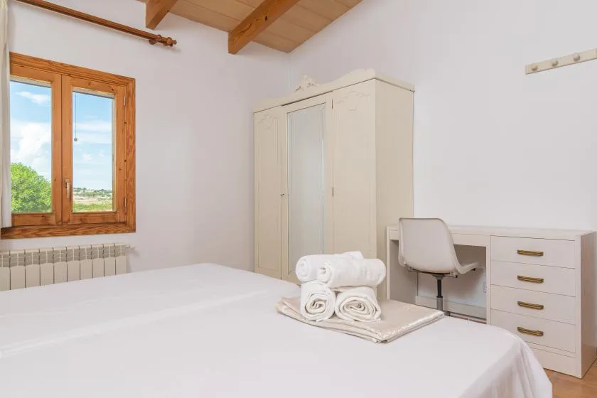 A bright bedroom with a bed, wardrobe, and desk beneath exposed wooden beams.
