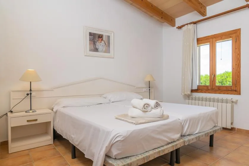 A bedroom with a double bed, bedside tables, and a wooden-framed window.