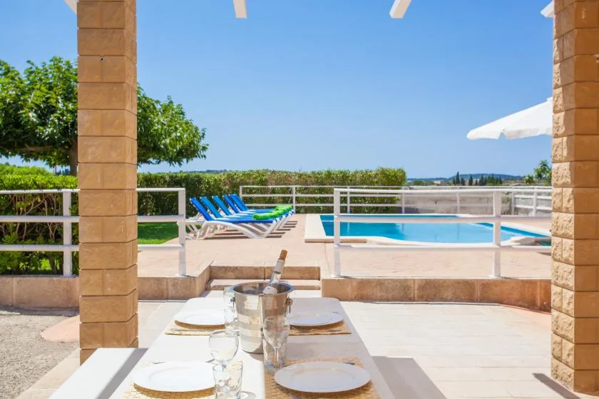 A poolside dining area overlooks a swimming pool, with lounge seating beyond.