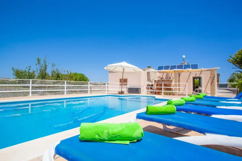 An outdoor swimming pool is lined with blue loungers and bright green cushions.