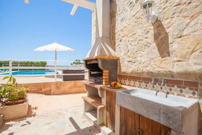 A sunny outdoor patio with a built-in grill and a stone sink beside the pool.