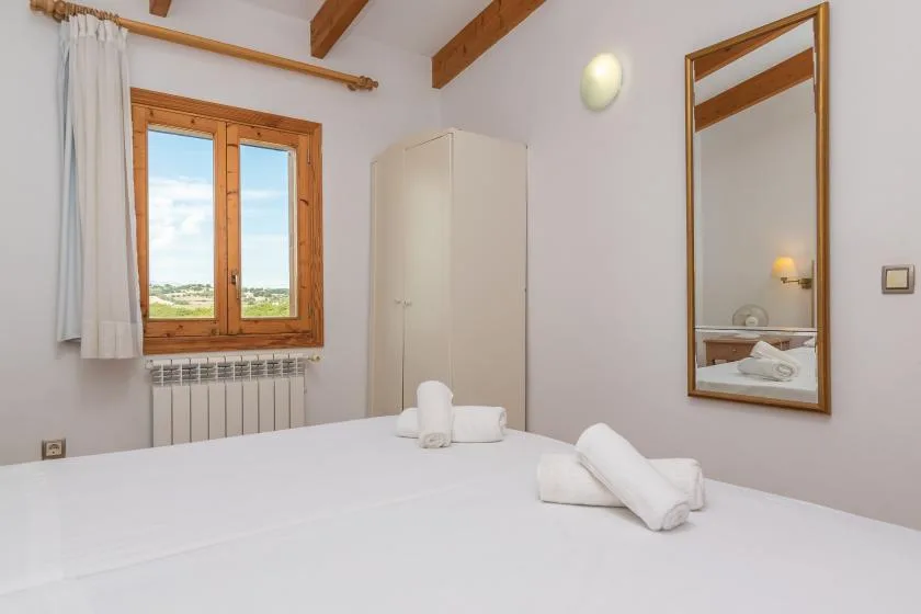 A bedroom with a neatly made bed, wooden-framed window, and wardrobe.