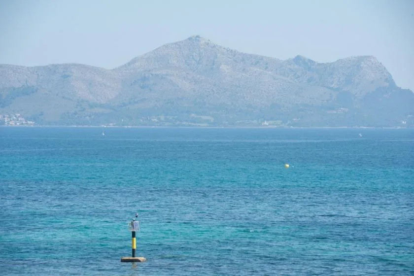 A blue sea stretches toward a mountainous coastline under a pale sky.